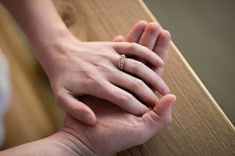 A groom's hand holding the bride's hand, wedding ring on her finger